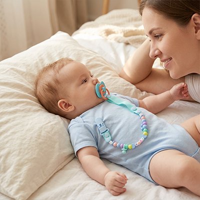 Attache tetine securibebe bebe sur le lit avec maman